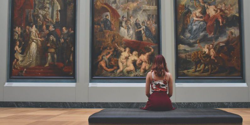 Museums - Woman Sitting on Ottoman in Front of Three Paintings