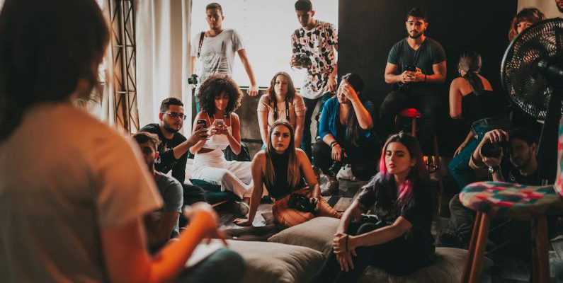 Community Events - Group of multiethnic people gathering around female speaker in studio