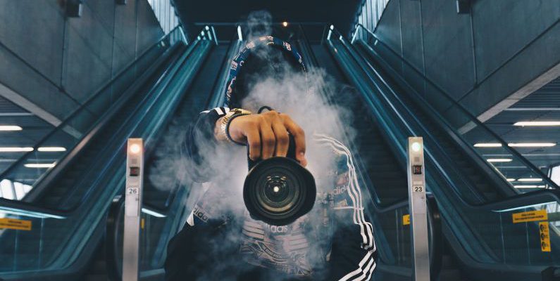 Photography - Man Holding Camera While Squating With Smoke on Face Inside Building