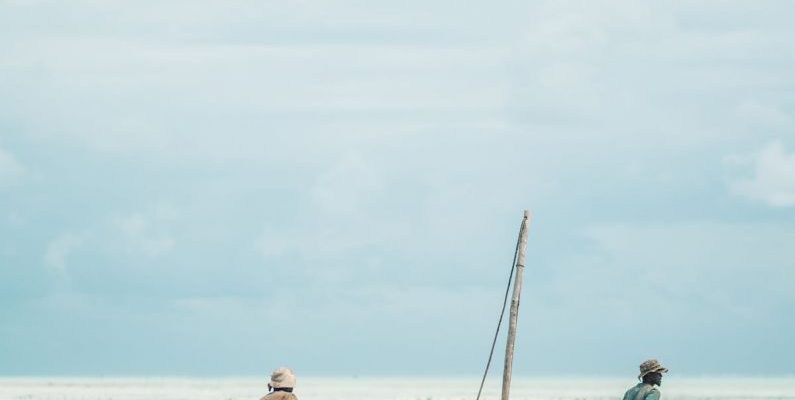 Locals - Two Men Dragging Wooden Boat on Sea Shore