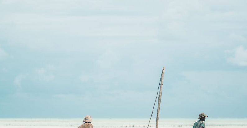 Locals - Two Men Dragging Wooden Boat on Sea Shore