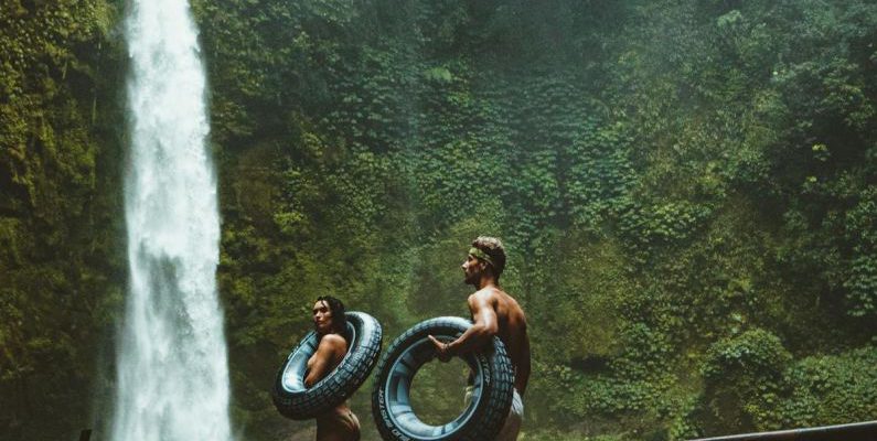Adventures - Two Person Carrying Black Inflatable Pool Float on Brown Wooden Bridge Near Waterfalls